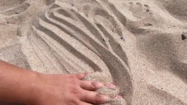 Mans hand scatters sand through his fingers. Hand movement