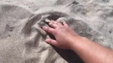 Mans hand scatters sand through his fingers. Hand movement