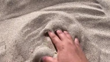 Mans hand scatters sand through his fingers. Hand movement