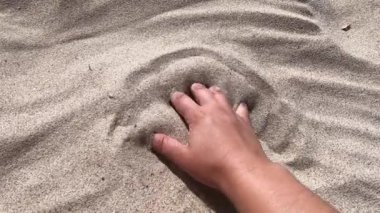 Mans hand scatters sand through his fingers. Hand movement