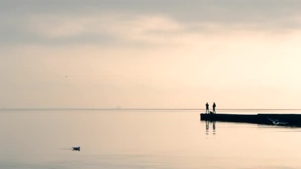 Dos hombres de pie y la pesca en un rompeolas en la mañana por la noche — Vídeos de Stock