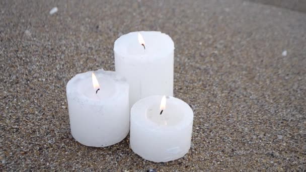 Three small white paraffin candles burning on sandy beach shore edge — Stock Video