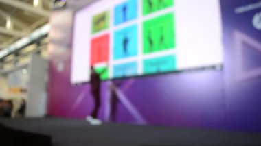 Man stands on stage. Blurred background large screen stage many people