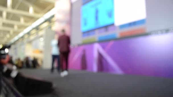 Man stands on stage. Blurred background large screen stage many people — Αρχείο Βίντεο