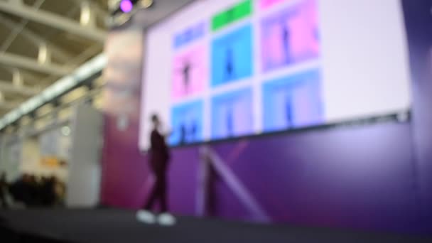 Man stands on stage. Blurred background large screen stage many people — Stockvideo