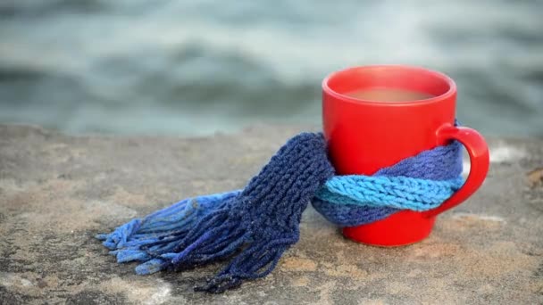 Red mug with coffee and steam tied with blue knitted scarf stands on stone — 图库视频影像