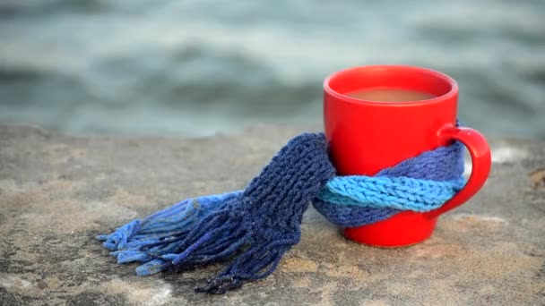 Červený šálek s horkým kávovým čajem, svázaný modrými pletenými stojany na šátky — Stock video