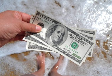 Deniz dalgalarının arka planında 300 dolarlık para tutan bir kız.