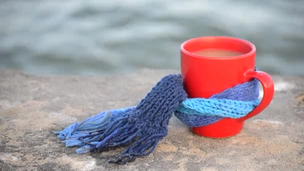 Tasse rouge avec café attaché avec écharpe tricotée bleue se tient sur la surface de la pierre — Video