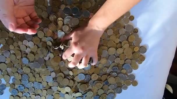 Person two hands rakes coins on table and pours spills from handful to surface — Stock Video