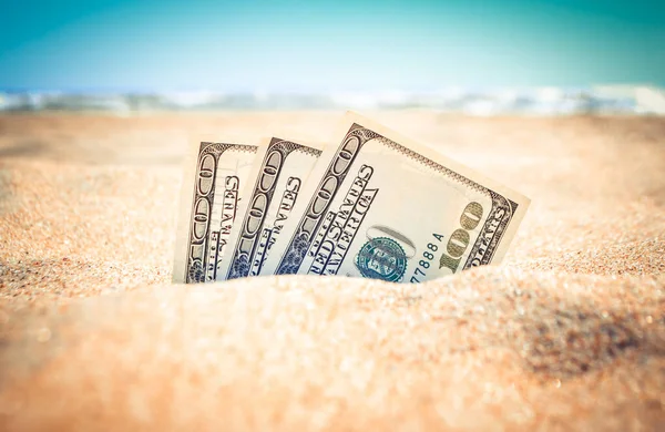 Peníze dolary napůl pokryté pískem leží na písečné pláži v blízkosti moře Stock Snímky