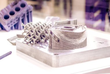 Metal 3D yazıcıya yazdırılmış nesneyi tutan adam.