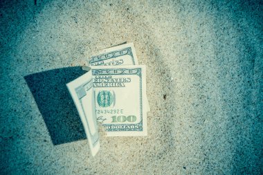 Paranın yarısı kumla kaplı, yakın planda yatıyor. Dolar banknotları kısmen kuma gömülmüş. Okyanus sahilinde kumlara gömülü 300 dolar. Finans parası hariç. Tatilde rahatla.