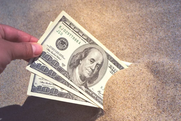 A girl takes out from the sand money notes of three hundred dollars. Concept finance money holiday relax vacation. Sunny summer warm day. A man takes out dollars from sand buried money banknotes