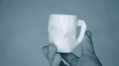 Kişi ellerini tutar ve 3D yazıcıda yaratılan beyaz nesneye bakar.
