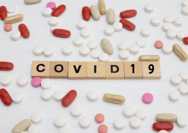 Üzerinde covid-19 yazan şırınga ve yanında çeşitli renkli tabletler var.