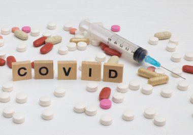 Üzerinde covid-19 yazan şırınga ve yanında çeşitli renkli tabletler var.