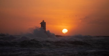 The Mangiabarche lighthouse wrapped in the waves of a mistral wind storm in a beautiful sunsetThe lighthouse was built over the rock from which it takes its name and located a short distance from the north-western coast of the Island of Sant'Antioco clipart