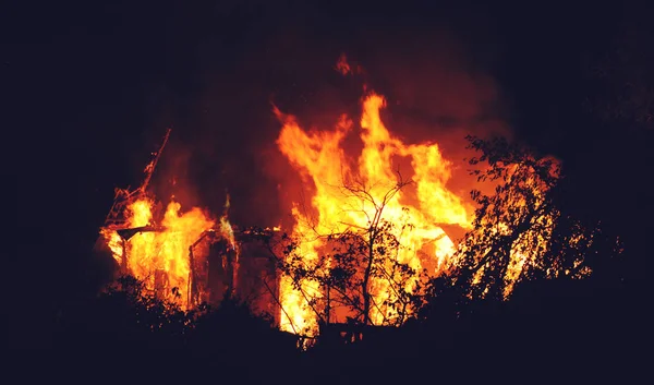 Arson or nature disaster - burning fire flame on wooden house roof. Big fire at night — Stock Photo, Image