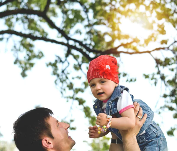 Ojciec wyrzuca na ręce małą córeczkę, na terenie parku na zachód słońca — Zdjęcie stockowe