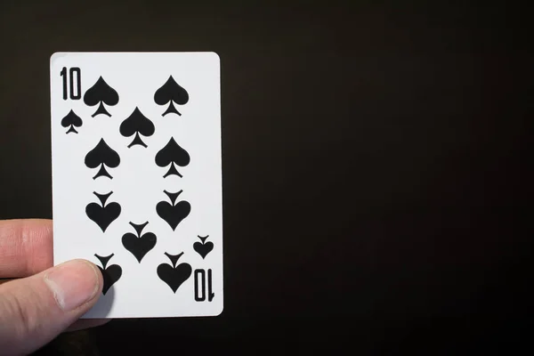 Résumé : main d'homme tenant la carte à jouer dix pique sur un fond noir avec copyspace — Photo