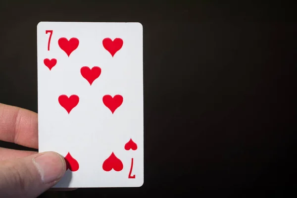 Resumen: mano de hombre sosteniendo la carta siete de corazones sobre un fondo negro con copyspace — Foto de Stock