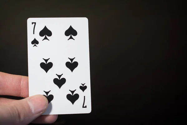 Анотація: рука людини тримає гральну картку сімох клубів на чорному тлі з копіспасом — стокове фото