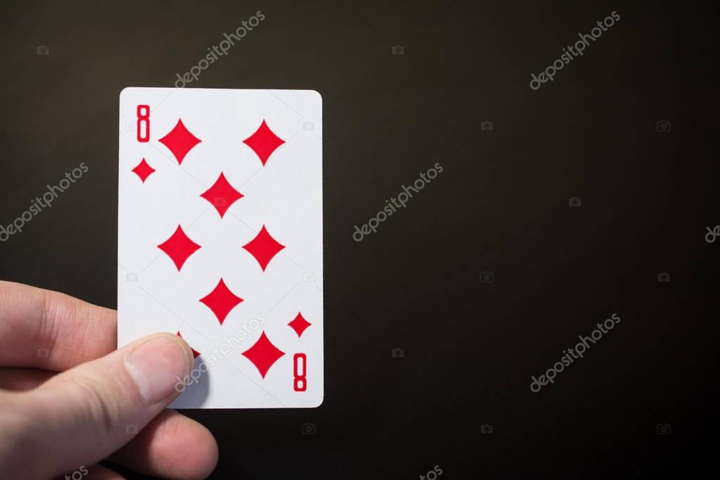 Man hand holding playing card eight of diamond isolated on black background with copyspace abstract