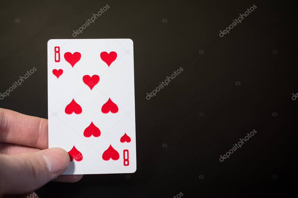 Man hand holding playing card eight of hearts isolated on black background with copyspace abstract