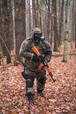 Elinde silah ve maskesi olan Rus askeri sonbahar ormanında duruyor.