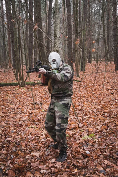 Russian soldier with a gun in his hands and a mask stands in the autumn forest
