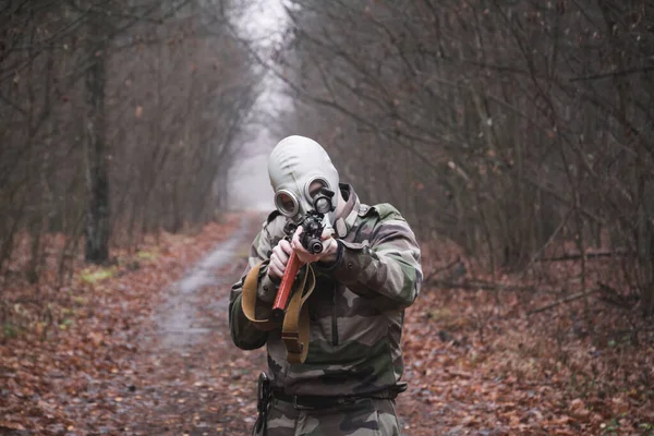 Żołnierz w kamuflażu i pistolet w ręku w lesie, w masce gazowej. — Zdjęcie stockowe