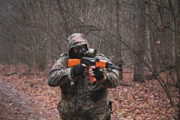 Żołnierz w kamuflażu i pistolet w ręku w lesie, w masce gazowej. — Zdjęcie stockowe