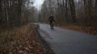 Silahlı bir adam Kalaşnikof saldırı tüfeği ve askeri kıyafetler giyiyor.