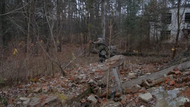 Imitatie van militaire operaties, twee militanten gewapend met Kalasjnikovs bewegen zich tactisch langs de ruïnes van een verwoest gebouw — Stockvideo