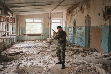 Terk edilmiş bir binada, cama silah doğrultmuş bir asker.