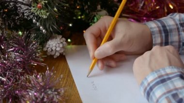 Bir adam Noel ağacının yanında ellerini uzatır ve Noel Baba 'ya yeni yıl mektubu yazar.