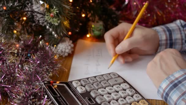 Um homem mãos perto de uma árvore de Natal decorada e considera o orçamento, o custo do Ano Novo ou presentes de Natal para sua família e colegas — Vídeo de Stock