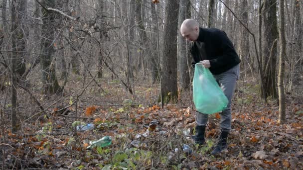 Волонтер собирает пластиковые бутылки, оставленные человеком в лесу в пластиковом пакете — стоковое видео