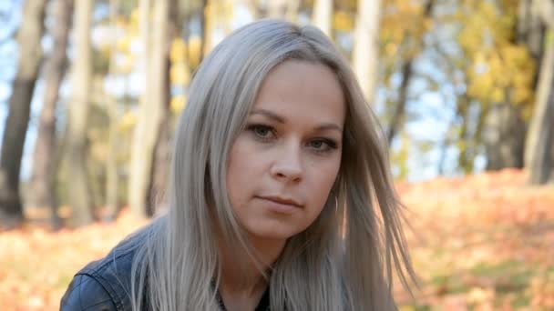 Retrato ao ar livre de uma menina bonita com cabelos brancos com uma expressão triste no fundo de folhas caídas — Vídeo de Stock