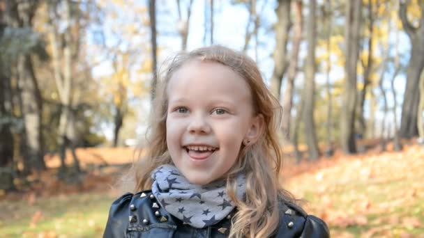 Alegre retrato de una hermosa niña de cinco años en el parque de otoño sobre un fondo de follaje amarillo — Vídeo de stock