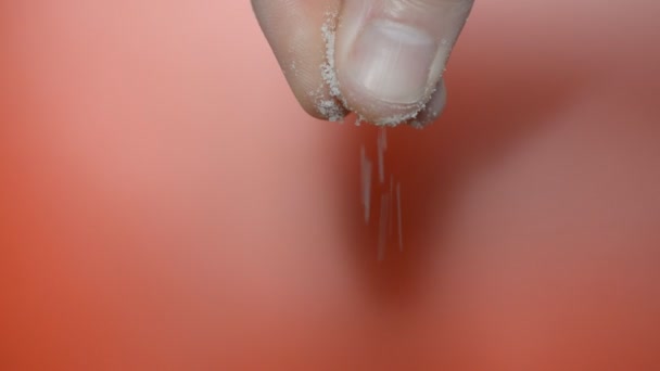 Мужская рука, пальцы обильно солят что-то на красном фоне — стоковое видео