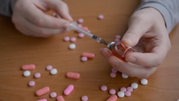 Las manos de un drogadicto preparan de cerca una jeringa inyectable de heroína sobre un fondo de una mesa con tabletas dispersas — Vídeos de Stock
