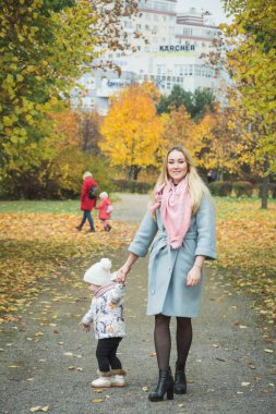 Anne bakımı kavramı, anne ve küçük kızı sonbahar caddesinde el ele yürüyorlar.