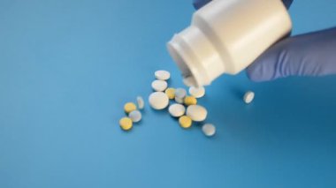 White bottle with multicolored tablets that fall on the blue background, treatment of coronavirus concept