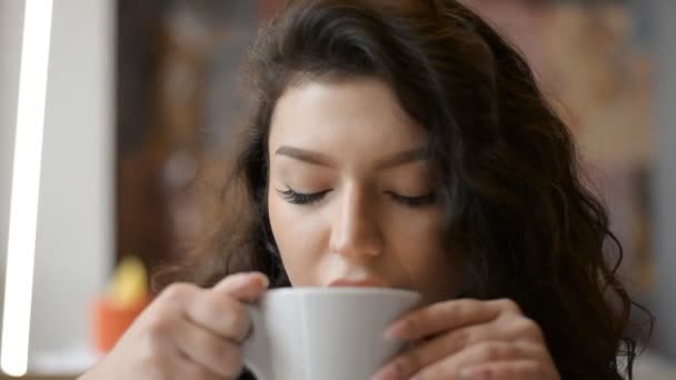 Hermosa chica de cabello castaño bebe un delicioso y amargo capuchino en un restaurante — Vídeo de stock