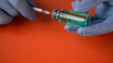 Doctors hands in blue gloves picks up a coronovirus COVID-19 vaccine in a syringe on a red background