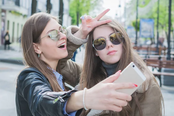 İki güzel genç kadın fotoğraf çekerken eğleniyor ve cep telefonuyla yüzünü buruşturuyor, yaşam tarzı kavramı.