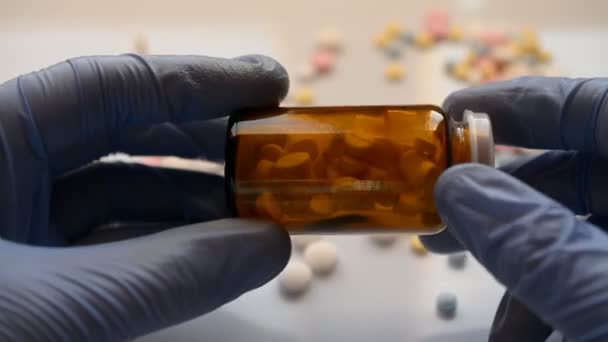 Lékaři ruce v modrých gumových rukavicích držet skleněnou pilulku láhev proti koronavirové infekci — Stock video