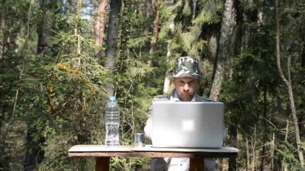 Человек, работающий на ноутбуке в лесу за столом — стоковое видео